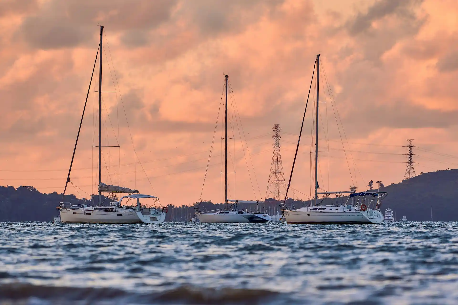 Three sailboats anchored in a calm bay at sunset, their silhouettes against a dramatic sky, prompting questions about whether do houseboats hold their value.