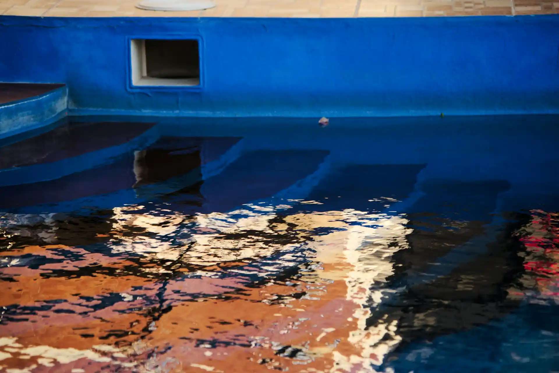 The deep blue interior of a swimming pool with visible steps, subtly reflecting surrounding colors, alluding to the corrosive environment of saltwater and how does saltwater affect boat paint.