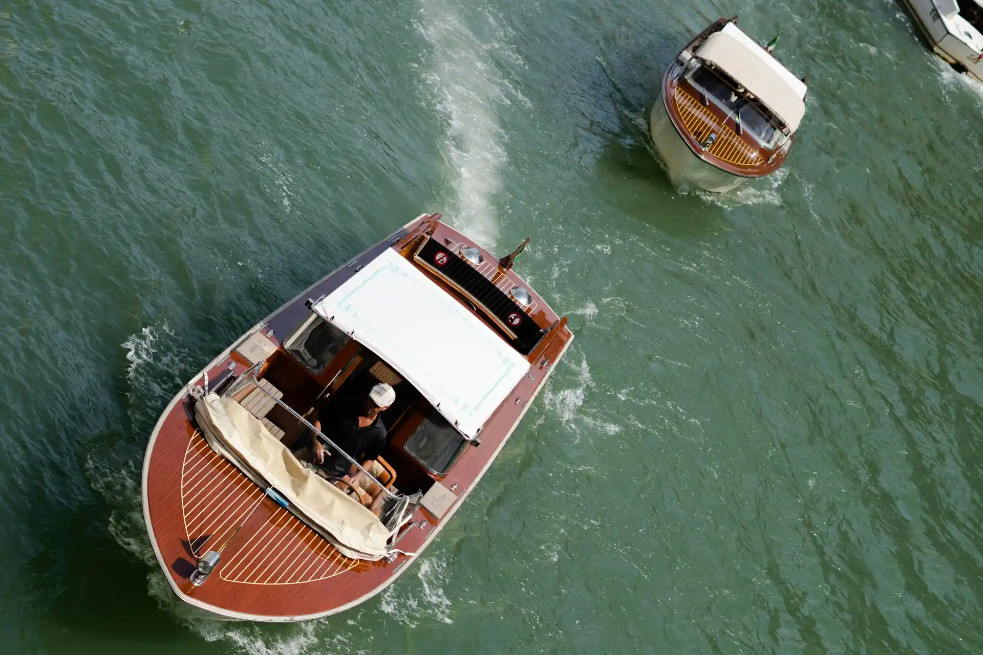 An overhead view of a classic wooden boat with a white cabin moving on water, and another boat nearby, illustrating a vessel that clearly answers the question, Do houseboats have engines?